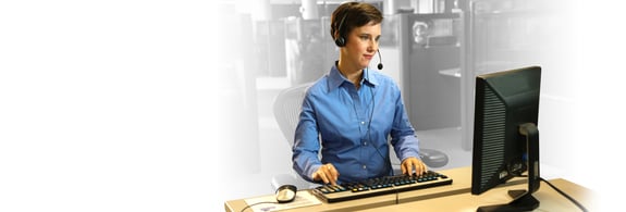 Adult female wearing a headset at her computer assisting customers.