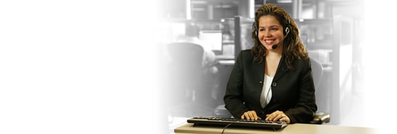 Adult female wearing a headset at her compter. She is ready to assist customers.